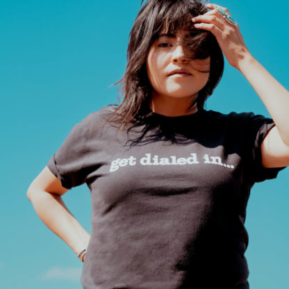 a woman is posing, wearing a black "get dialed in..." T-shirt
