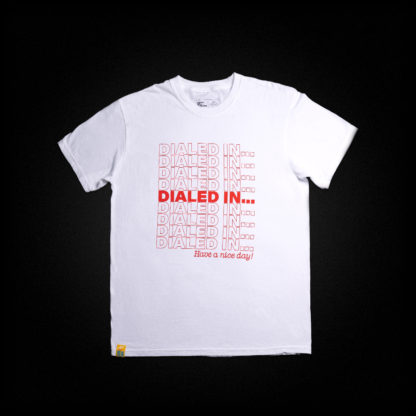 a white shirt is laid flat; printed on it is a red graphic that says "Dialed In..." repeatedly and "Have a Nice Day!" underneath