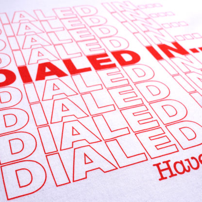 close-up view of a screen printed red graphic on a white T-shirt that says "Dialed In..." repeatedly and "Have a nice day!" underneath