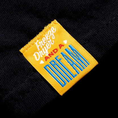 front of a yellow sewn-on tag on a black shirt that says "Freeze Dryer and a Dream"